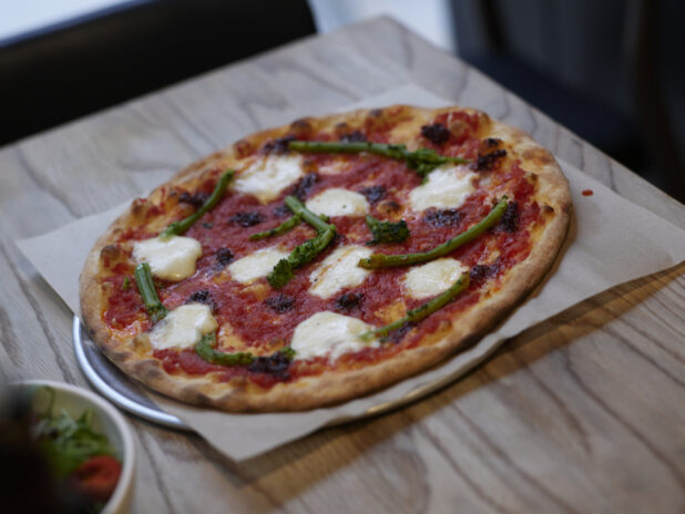 A thin crust Neapolitan-style Margherita Pizza with rapini on parchment paper