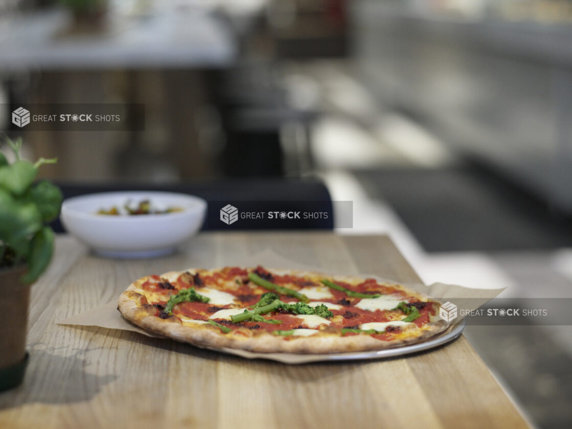 A Neapolitan-style Margherita pizza with rapini on a wood counter in a kitchen