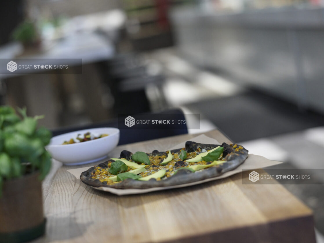 Ikasumi Pizza with avocado and basil on a wood table, close-up, low angle