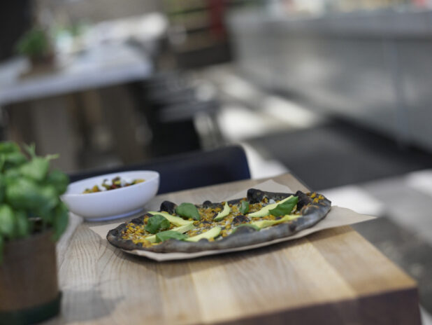 Ikasumi Pizza with avocado and basil on a wood table, close-up, low angle