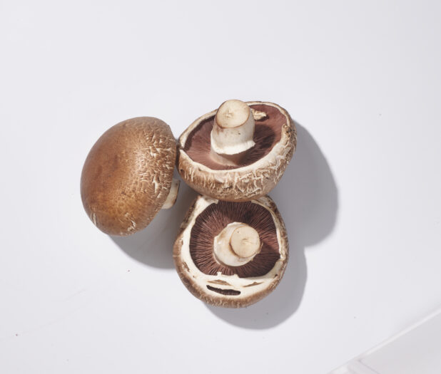 Whole fresh cremini mushrooms on a white background