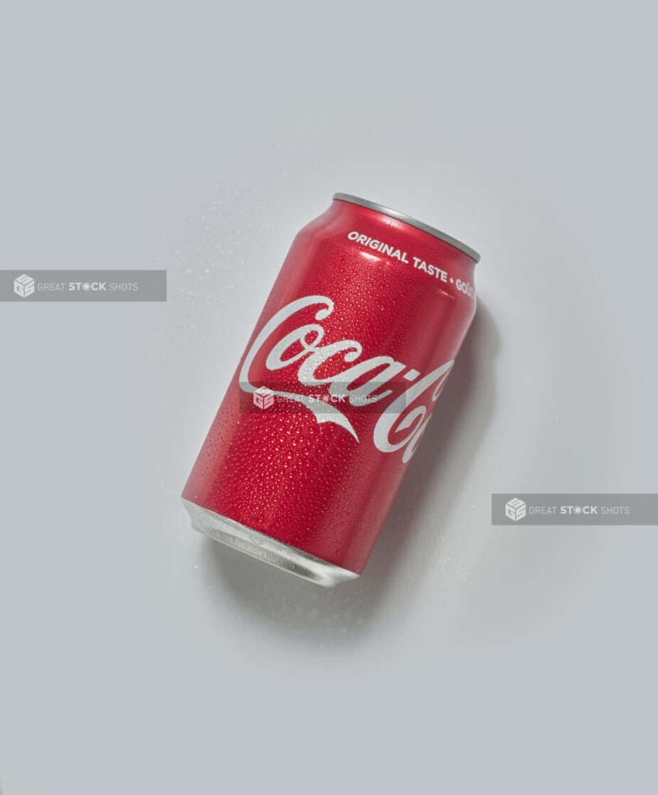 A cold can of Coca-Cola on its side on a white background, tilted