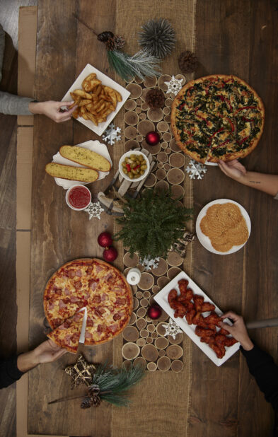 A family at a dinner table decorated for Christmas with pizza and buffalo wings