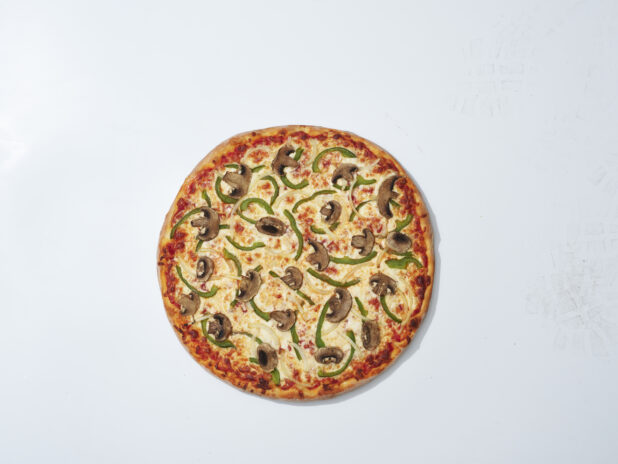Whole unsliced New York style vegetarian pizza on a white background