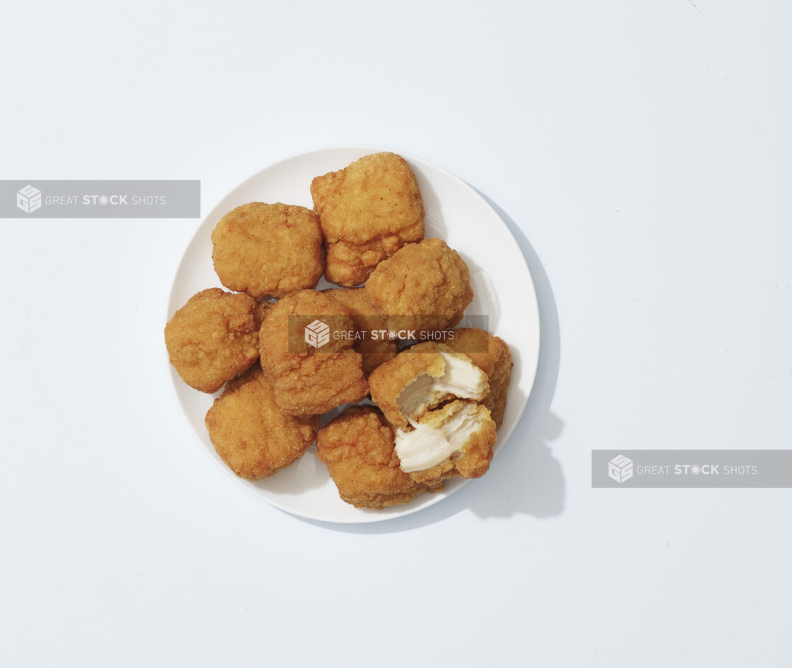 A pile of chicken nuggets with one torn open on a white plate on a light background