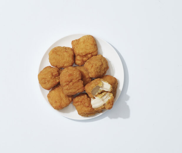 A pile of chicken nuggets with one torn open on a white plate on a light background