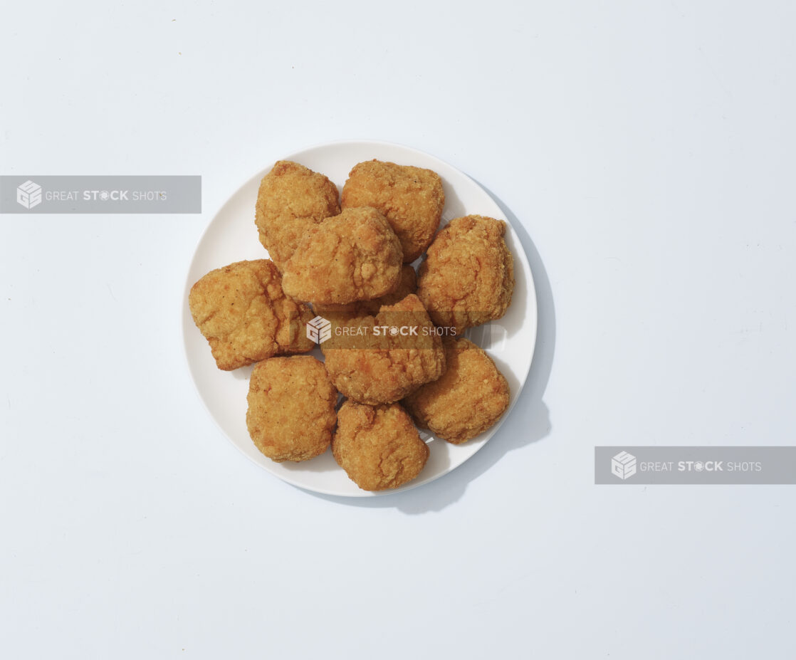 A mound of chicken nuggets on a white plate on a light background