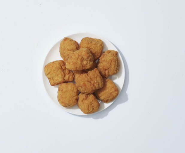 A mound of chicken nuggets on a white plate on a light background