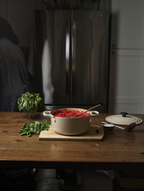 A French cocotte full of tomato sauce with fresh basil on a wooden cutting board on a dark wooden table
