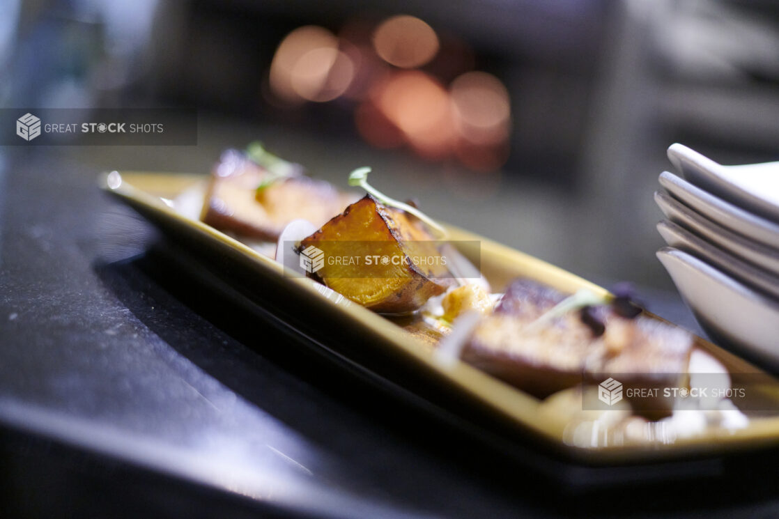 Roasted sweet potato on a rectangular platter with white side plates on a black background, close up view