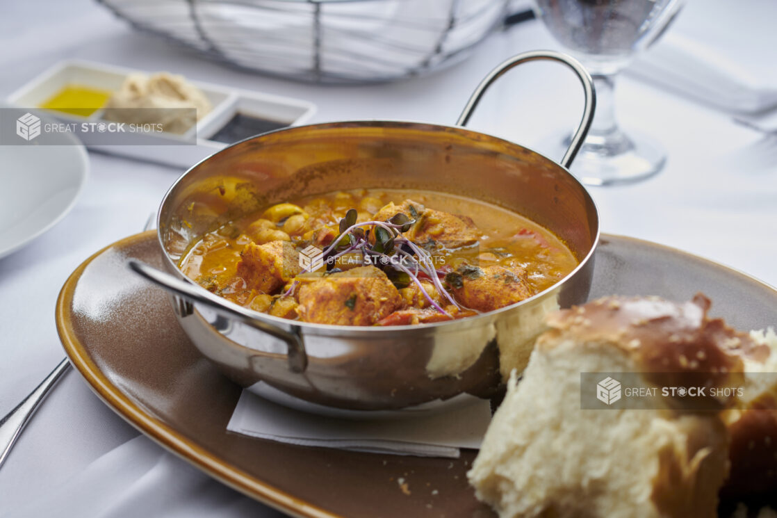 Butter chicken in a metal karahi bowl with bread on the side on a rustic ceramic plate on a white linen background