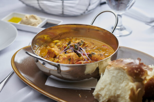 Butter chicken in a metal karahi bowl with bread on the side on a rustic ceramic plate on a white linen background