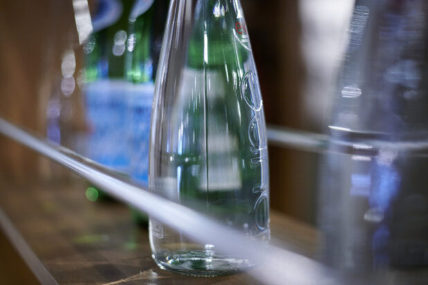 Clear glass bottled water on a wood shelf with other bottles surrounding