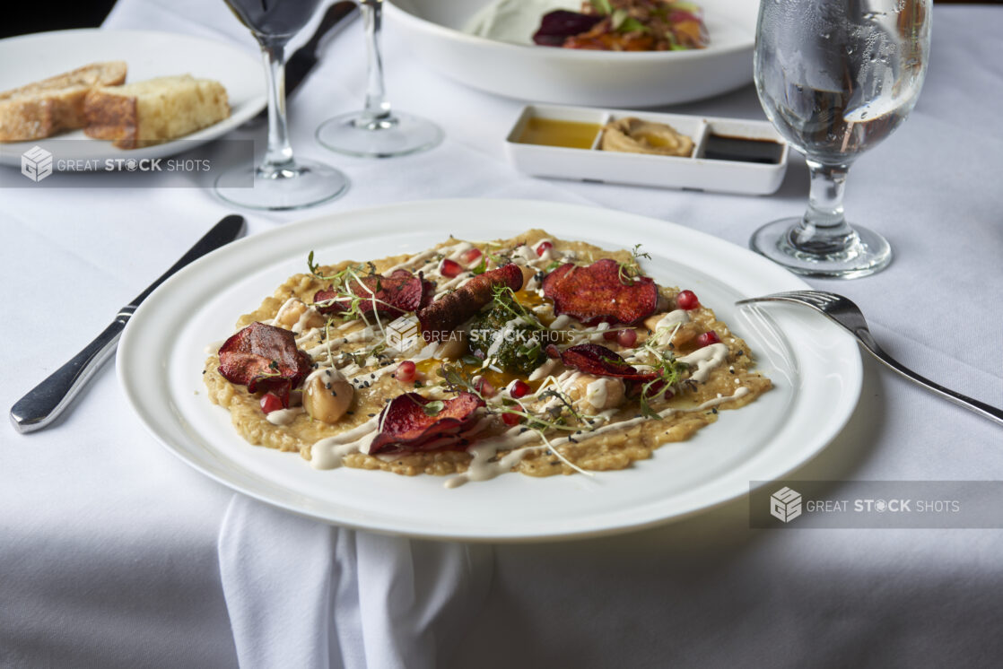 Roasted root vegetables and hummus appetizer on a white plate in a dining setting