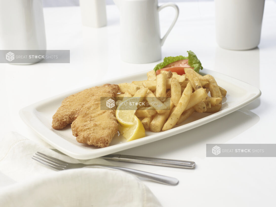 Battered fish and chips with lemon wedges on a white plate with a white background