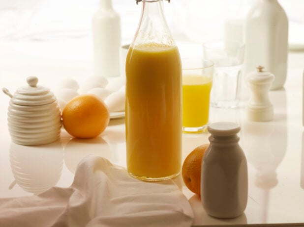 Glass jug of freshly squeezed orange juice with whole oranges on a white background