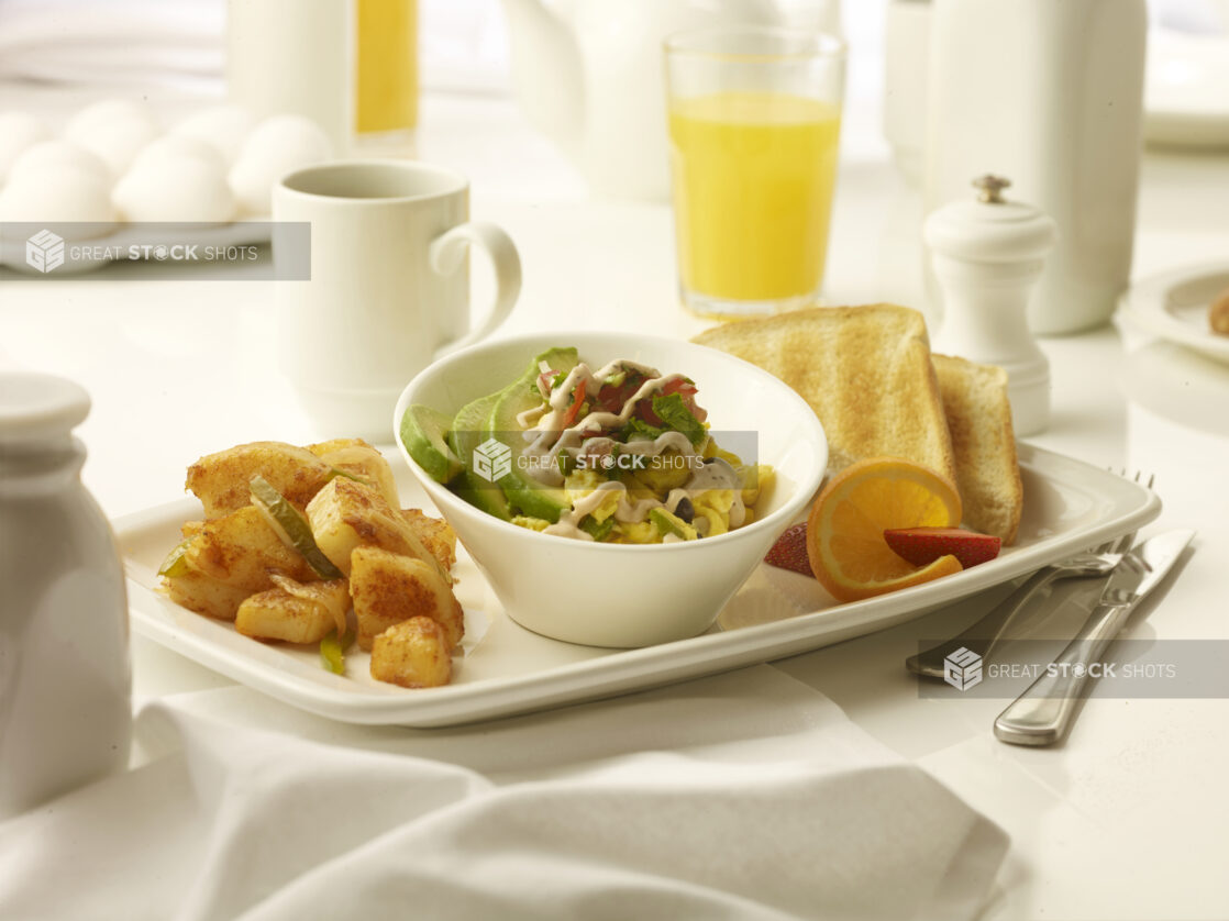 Breakfast bowl with a side of home fries and toast with a glass of orange juice and a cup of coffee in the background