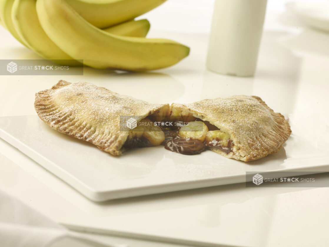 Chocolate and banana turn over cut in half on a white marble cutting board with whole fresh bananas in the background