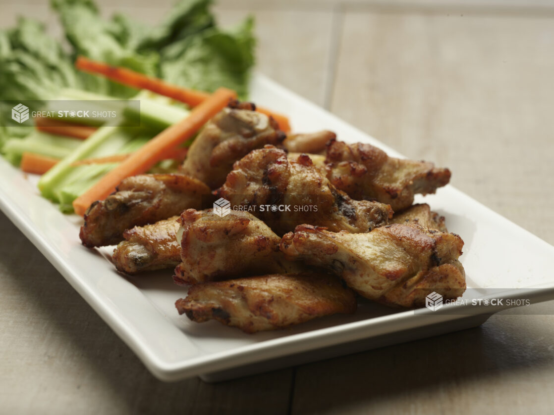 Naked chicken wings with celery and carrot sticks on a white plate with a wooden background