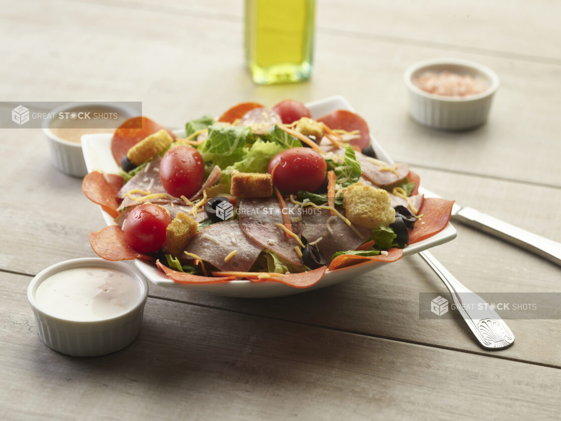 Deli meat garden salad with creamy sauce on the side on a wooden table