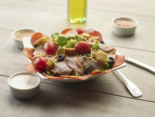 Deli meat garden salad with creamy sauce on the side on a wooden table