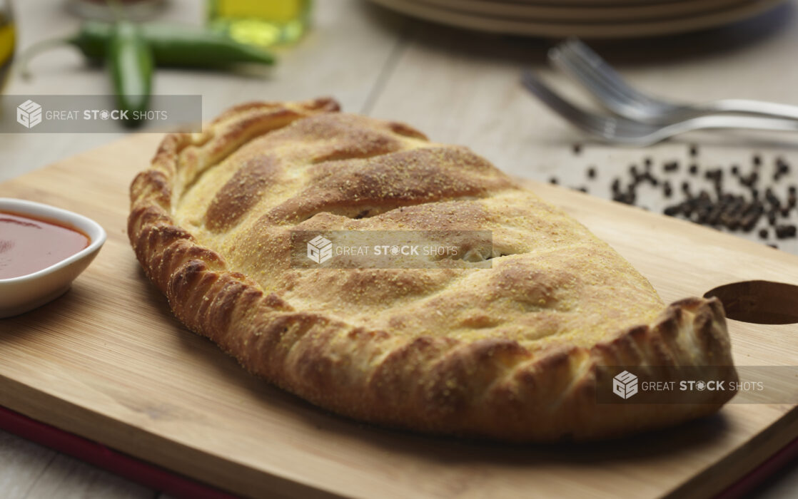 Whole panzerotti with a side of tomato sauce in a white ramekin on a wooden board