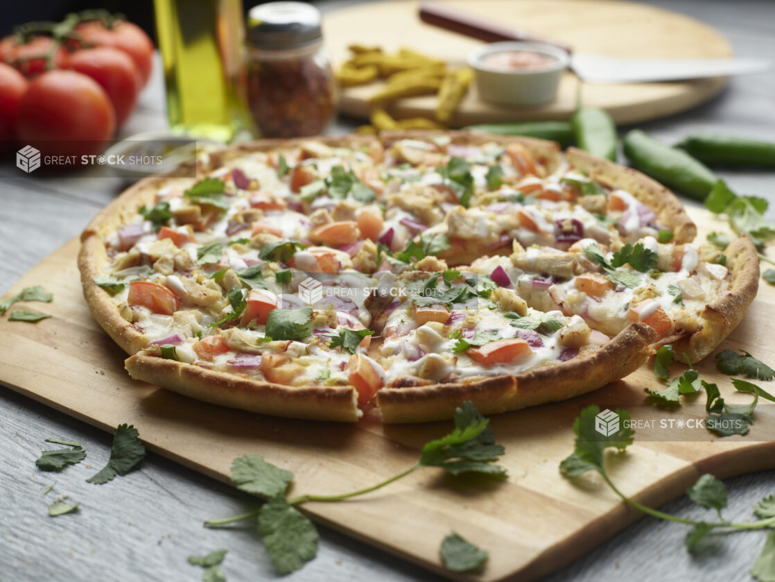 Sliced tandoori veggie pizza with mushrooms, red onion and tomatoes topped with fresh cilantro on a wooden cutting board surrounded by ingredients in the background