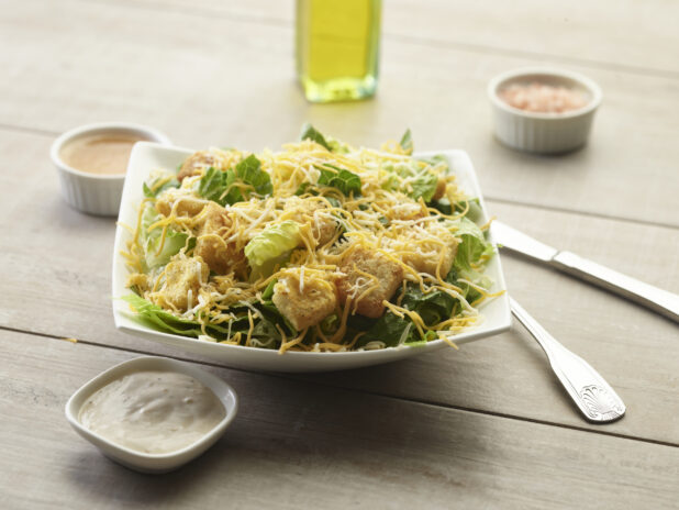 Cheesy Caesar salad with creamy sauce on the side on a wooden table