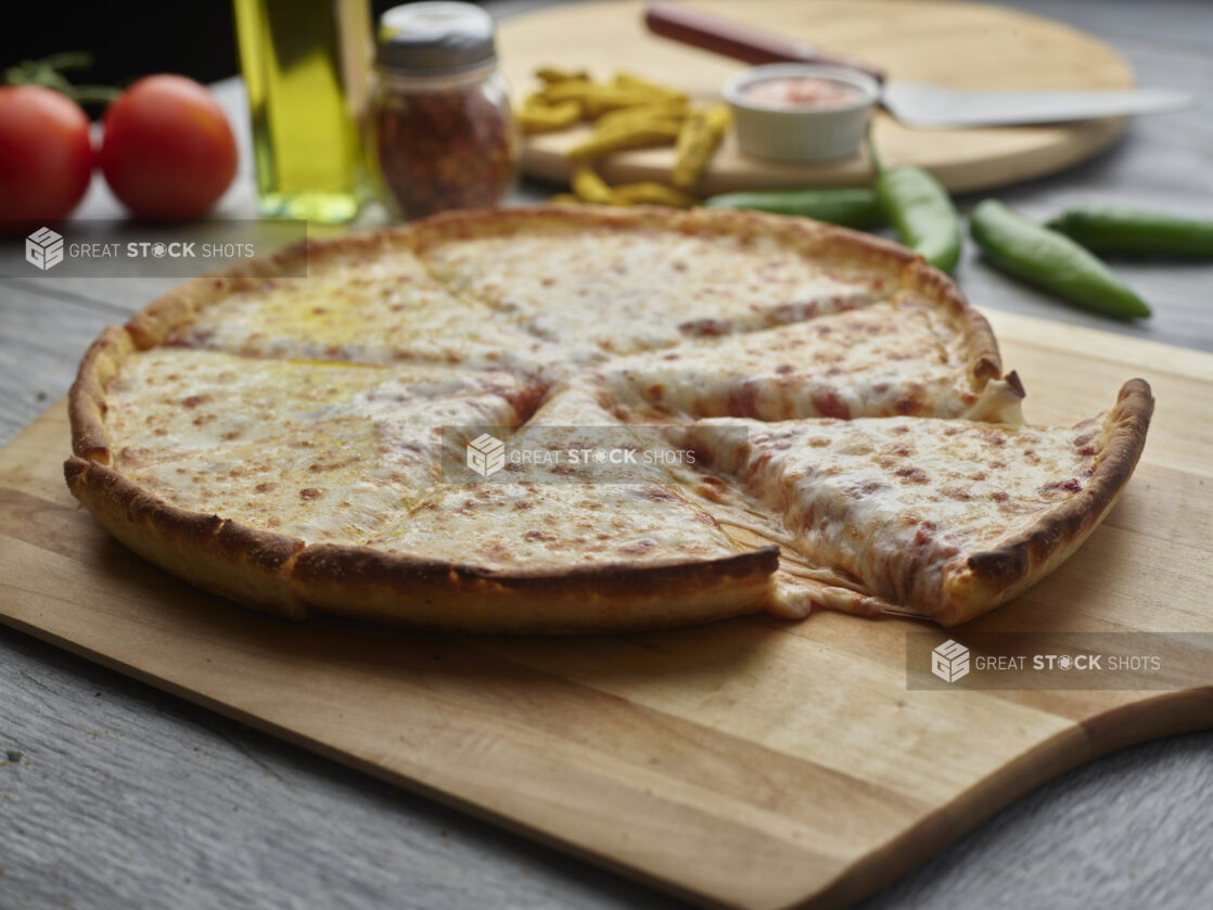 Sliced cheese pizza on a wooden peel surrounded by ingredients