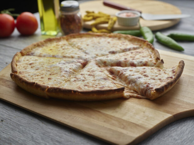 Sliced cheese pizza on a wooden peel surrounded by ingredients