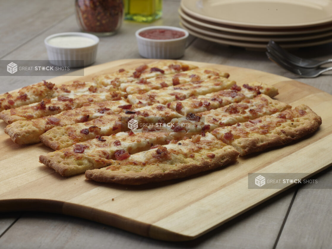 Sliced bacon flatbread on a wooden peel with a creamy and tomato dipping sauce in the background