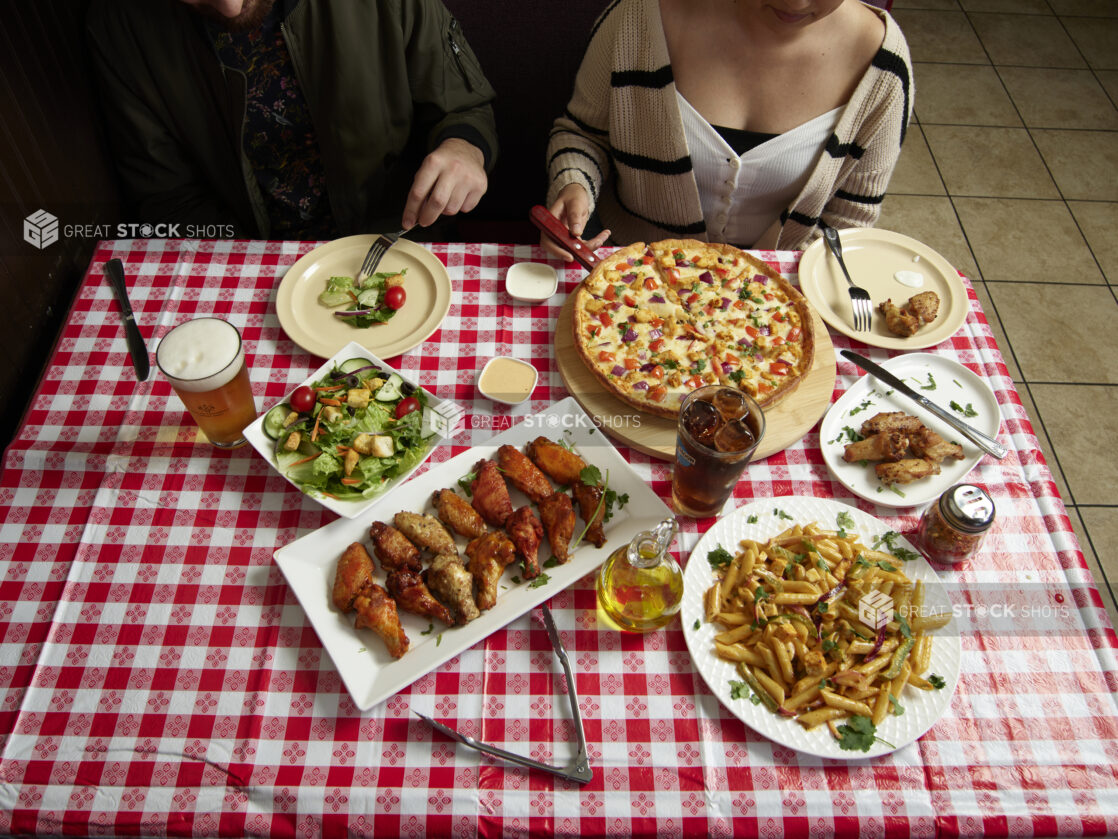 Couple at a restaurant with numerous dinner options on a red and white tablecloth in a restaurant