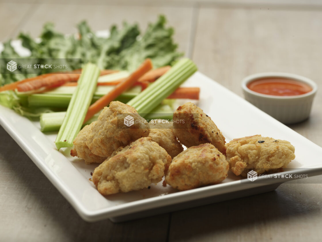 Plate of boneless chicken bites with celery and carrot sticks with a side of dipping sauce on a wooden background