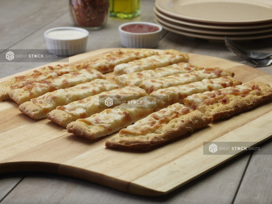 Sliced cheesy flatbread on a wooden peel with a creamy and tomato dipping sauce in the background