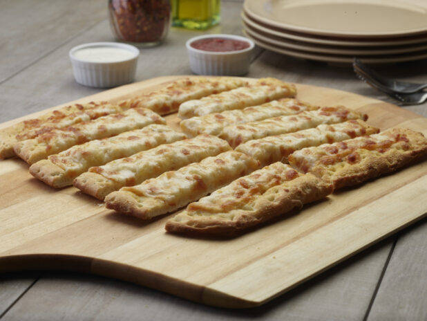 Sliced cheesy flatbread on a wooden peel with a creamy and tomato dipping sauce in the background