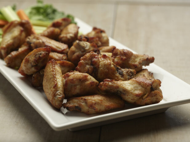 Naked chicken wings on a white plate on a wooden background