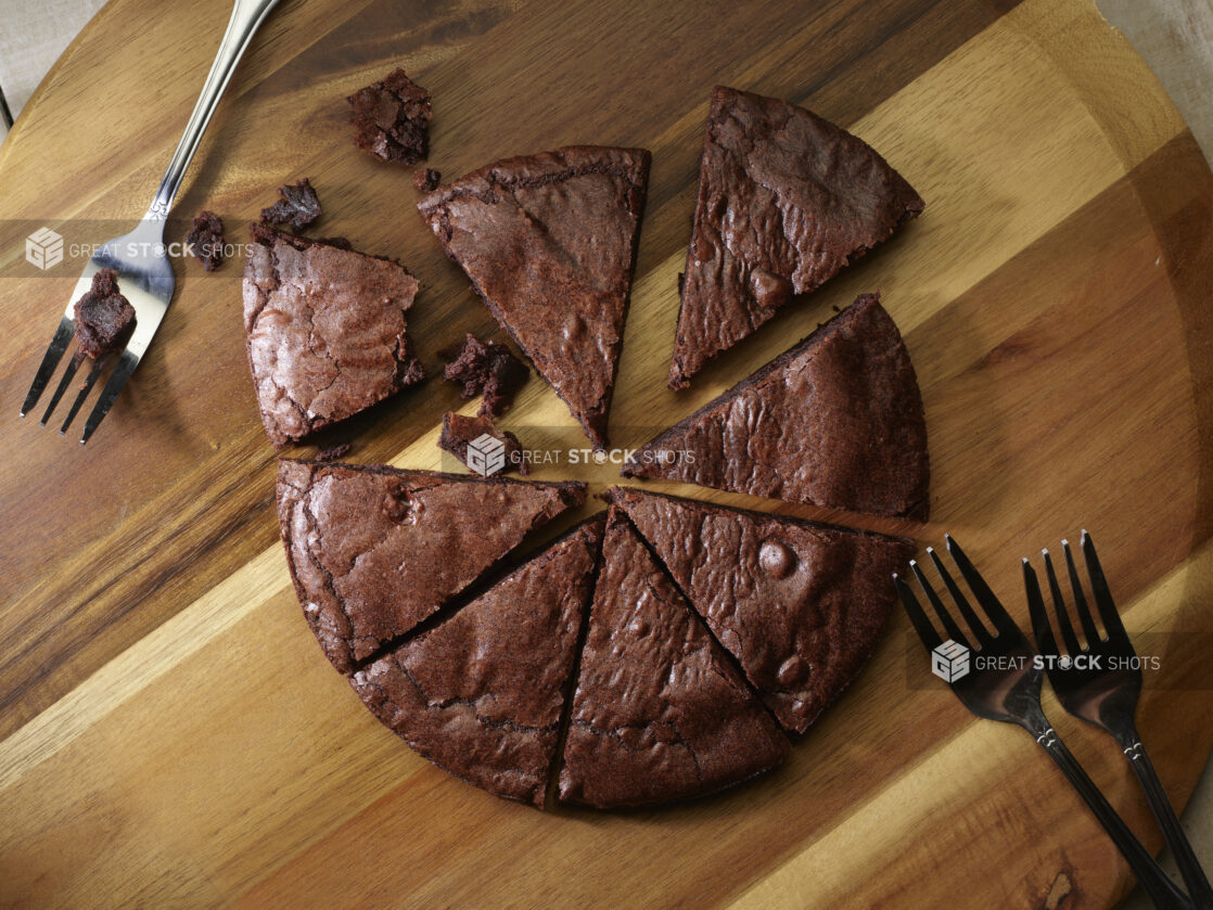 Overhead of a double chocolate cookie pizza cut into slices with forks for sharing on a wooden board