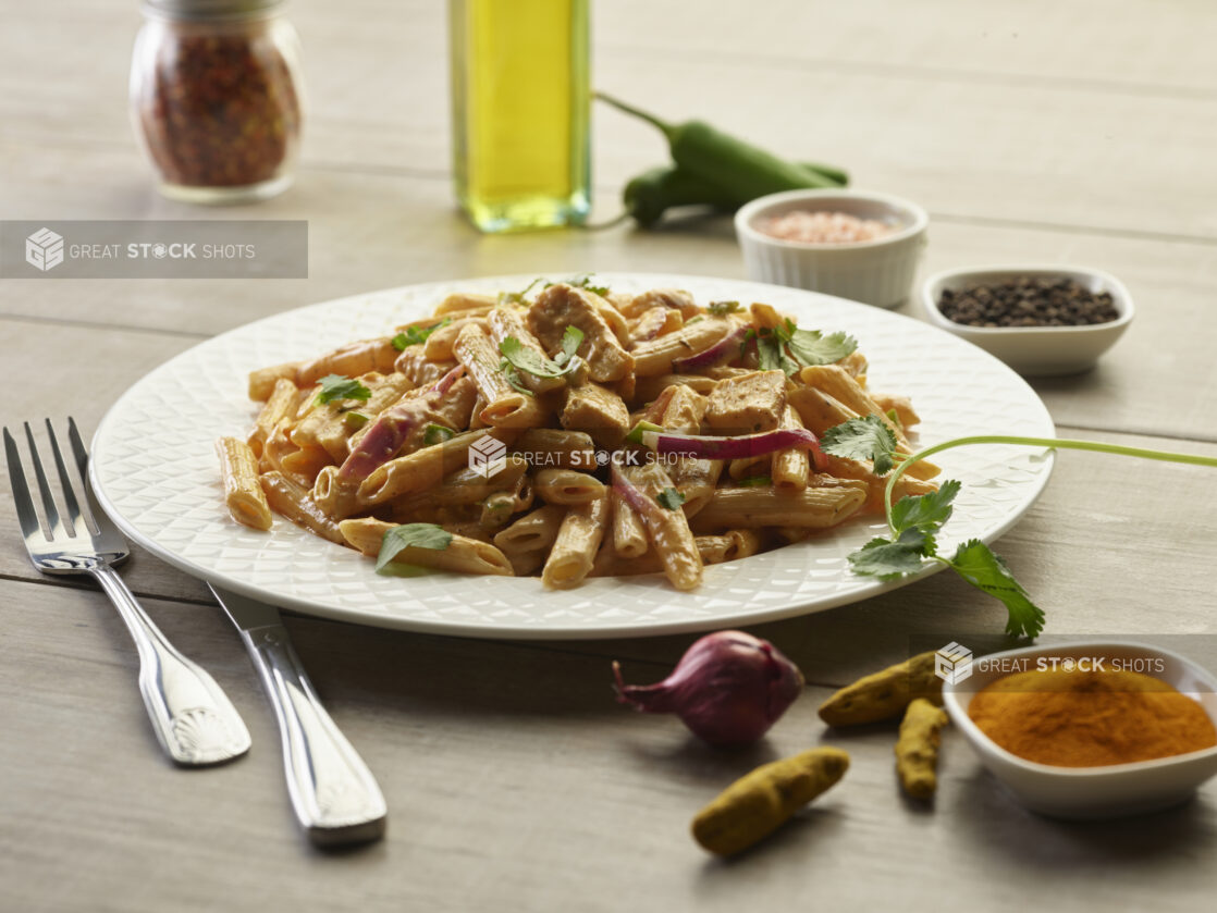 Palak Paneer pasta with peppers and red onions in a white bowl surrounded by ingredients on a wooden table