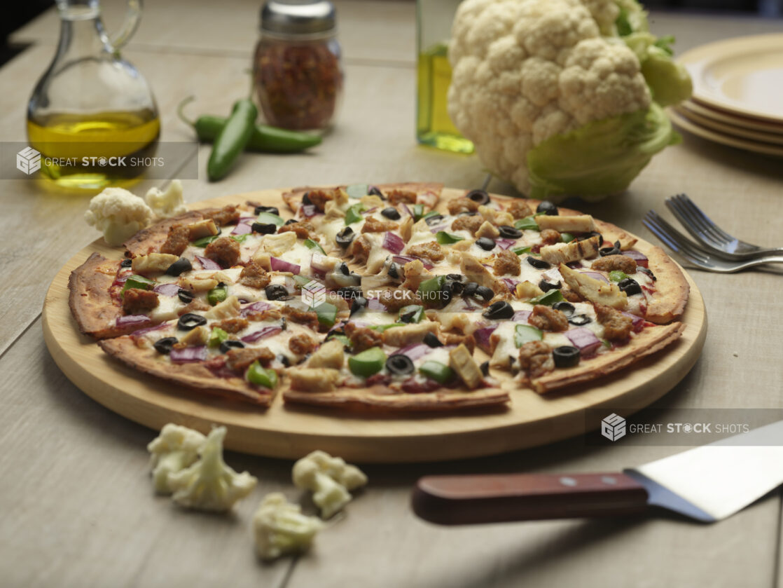 Sliced cauliflower crust pizza with four toppings on a wooden board with a whole raw cauliflower head in the background