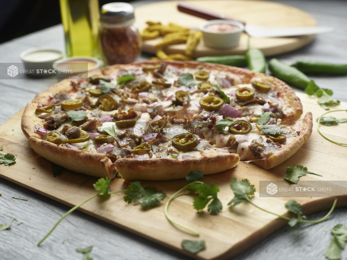 Sliced achari paneer pizza with red onion and jalapeño topped with cilantro on a wooden peel surrounded by ingredients