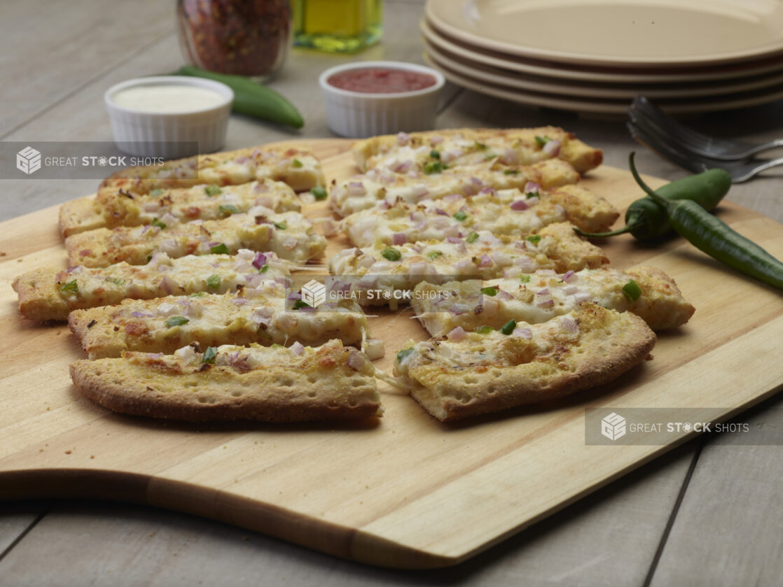 Sliced vegetarian flatbread on a wooden peel with a creamy and tomato dipping sauce in the background