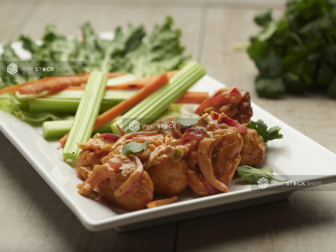 Plate of sauced boneless chicken bites with peppers and a side of celery and carrot sticks on a white plate