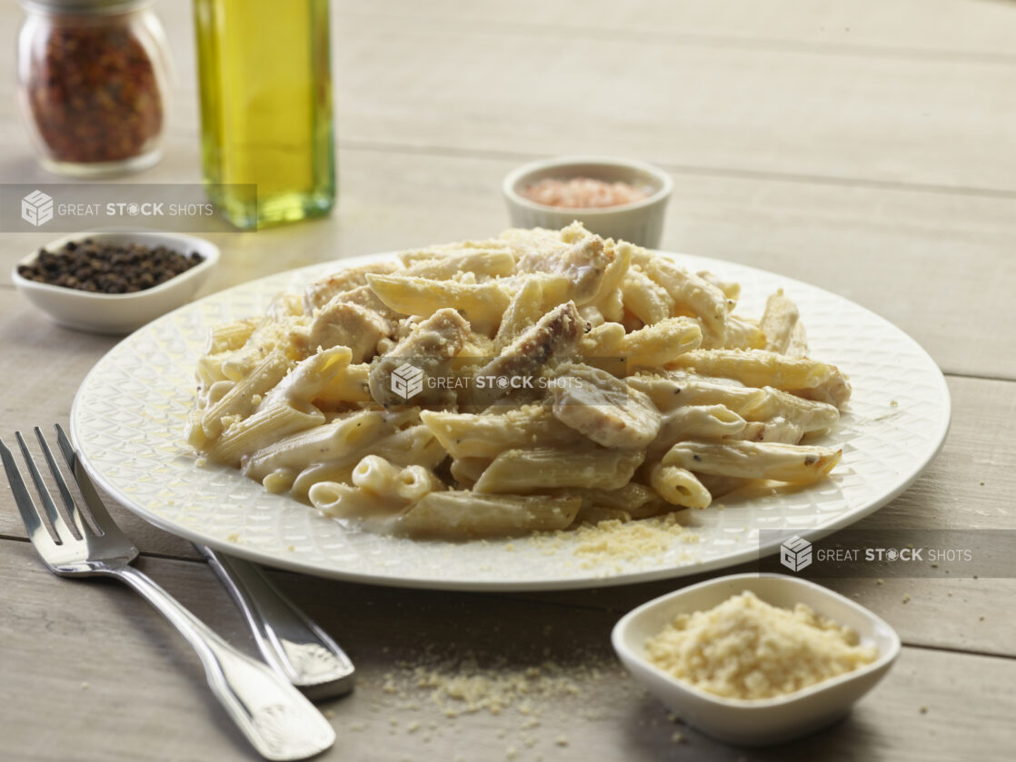 Chicken Alfredo penne pasta in a white bowl with topped with parmesan cheese on a wooden table