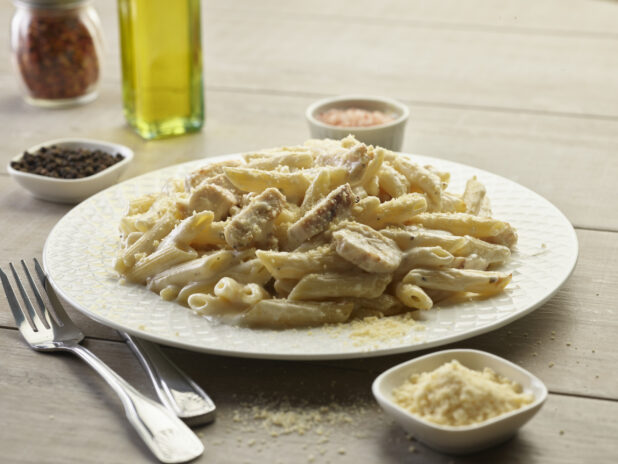 Chicken Alfredo penne pasta in a white bowl with topped with parmesan cheese on a wooden table