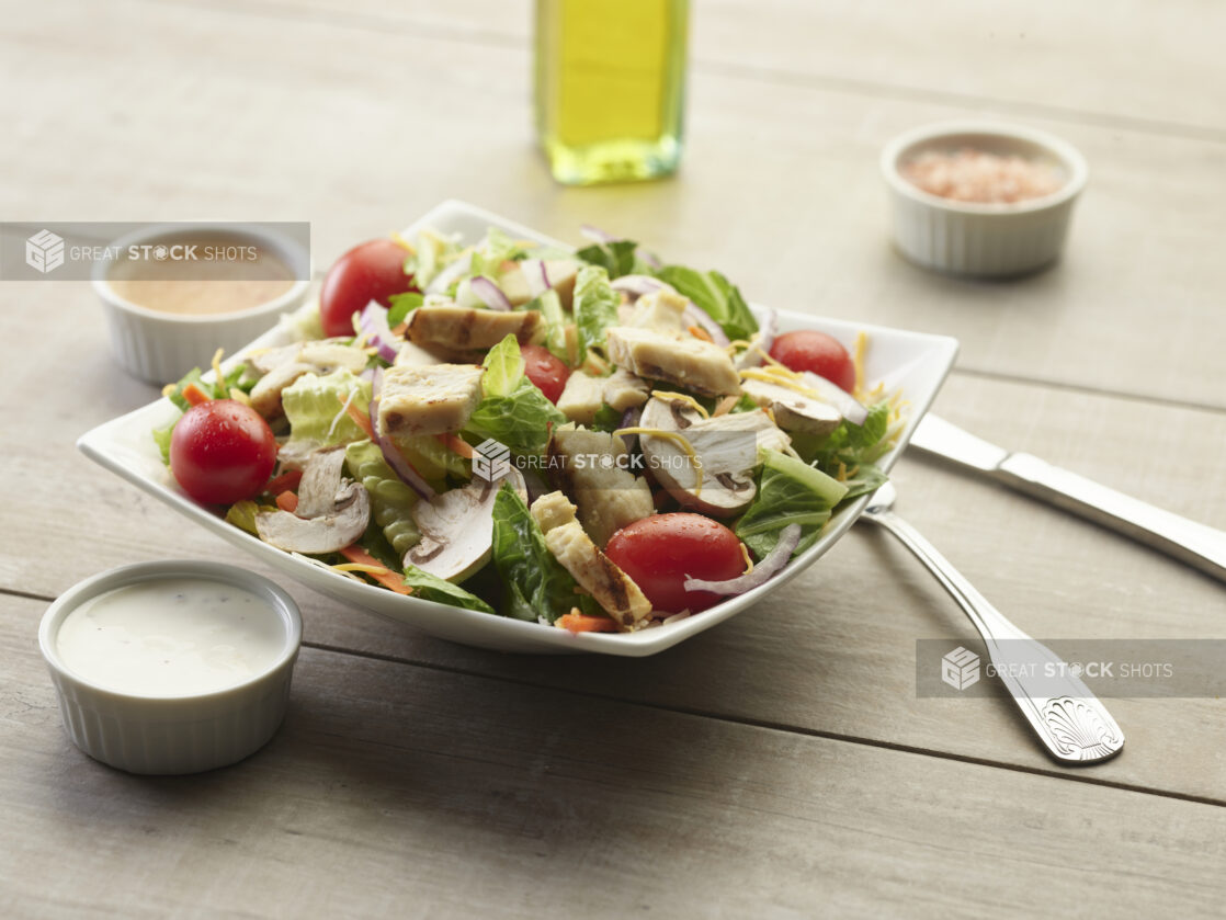 Chicken garden salad with creamy sauce on the side on a wooden table