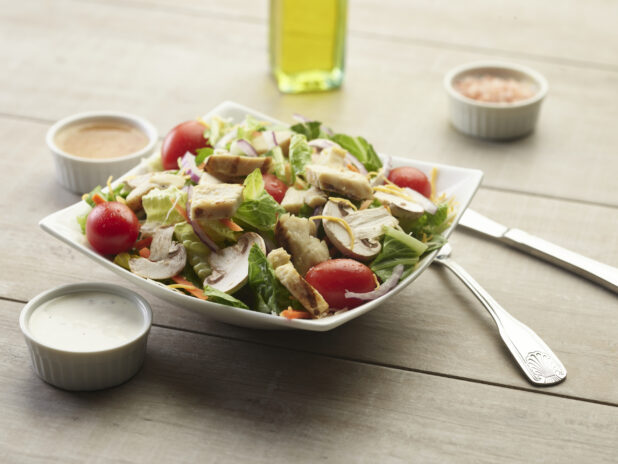 Chicken garden salad with creamy sauce on the side on a wooden table