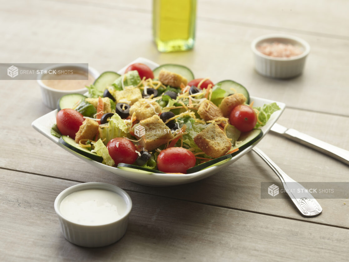 Garden salad with creamy sauce on the side on a wooden table