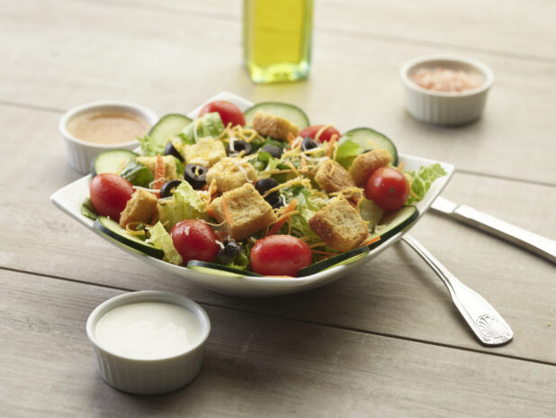 Garden salad with creamy sauce on the side on a wooden table