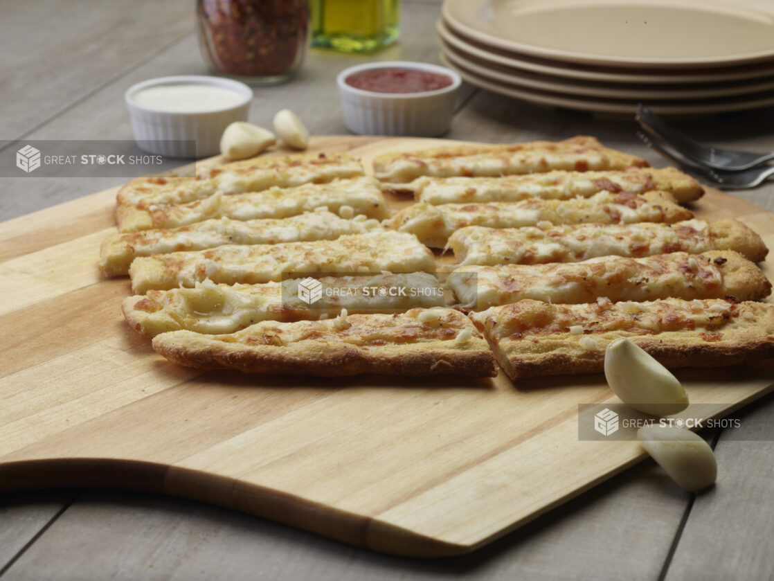 Sliced garlic bread flatbread with cheese on a wooden peel with a creamy and tomato dipping sauce in the background