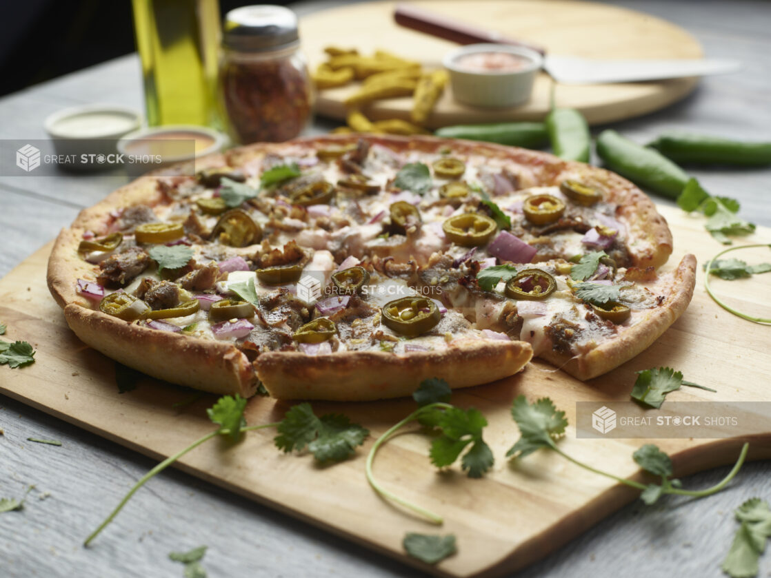 Sliced achari paneer pizza with red onion and jalapeño topped with cilantro on a wooden peel surrounded by ingredients